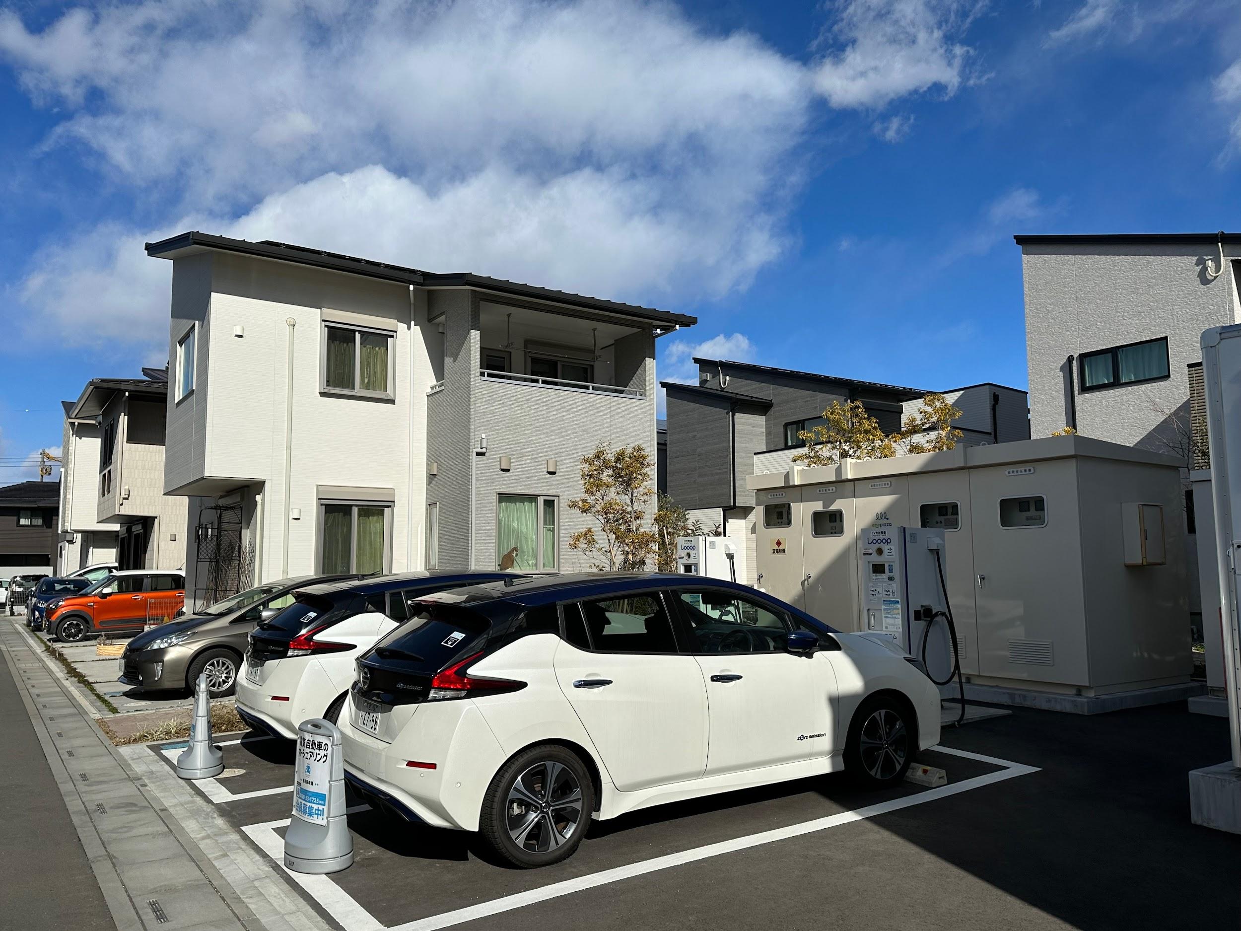 写真）「浦和美園E-フォレスト第3期」内のチャージエリア　2台のEV（日産リーフ）の前にある設備は受変電設備。蓄電池やEV、商用系統からの電気を各住戸へ供給する。カーシェアリング用EV（日産リーフ）は、平日は蓄電池として街区のエネマネに活用（40kWh×2）し、土日はシェアカーとして住民が利用できる。